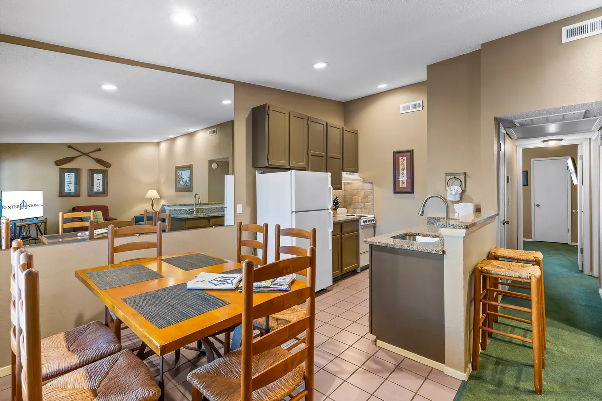 An open-plan interior seamlessly connecting the kitchen and dining area. The image features a cozy dining table, kitchen amenities, bar stools, and a glimpse of the living area, evoking warmth and togetherness.