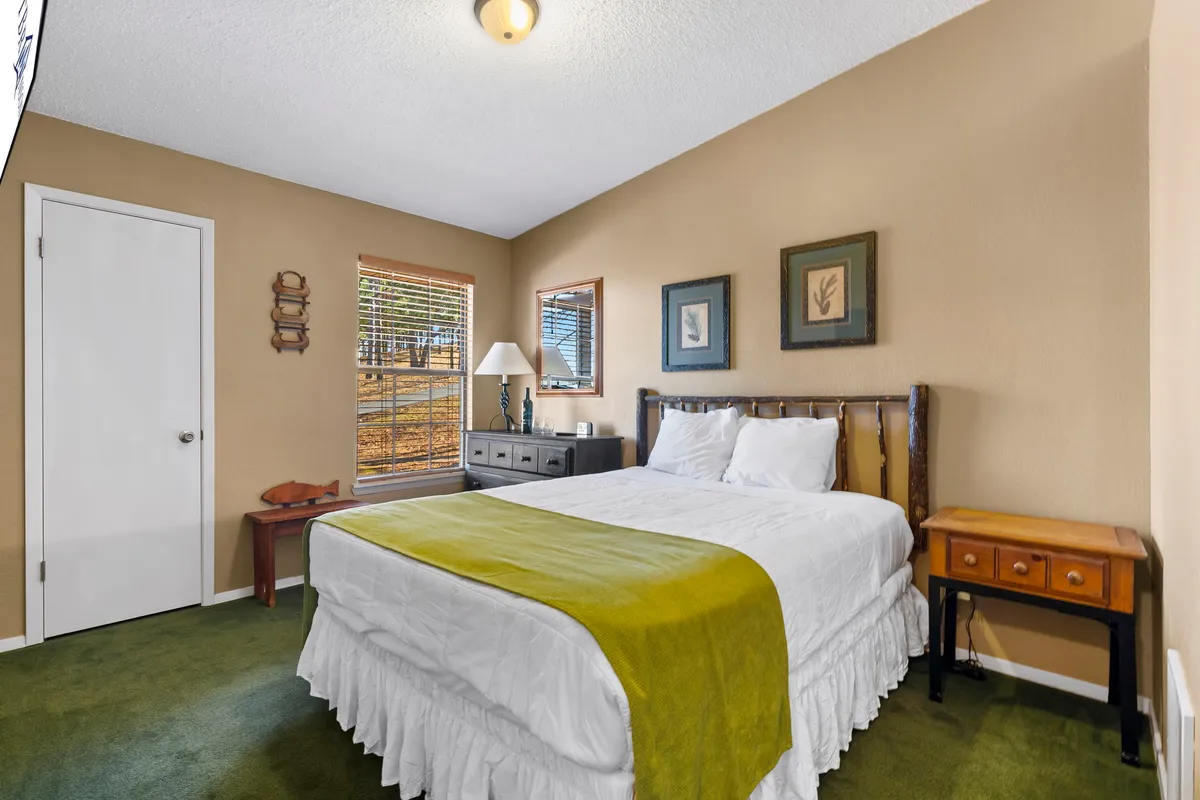 A cozy bedroom with a large window, king-sized bed, elegant nightstand, and vibrant artwork on the wall. Sunlight streams in, creating a warm, welcoming space ideal for unwinding and enjoying a private retreat.