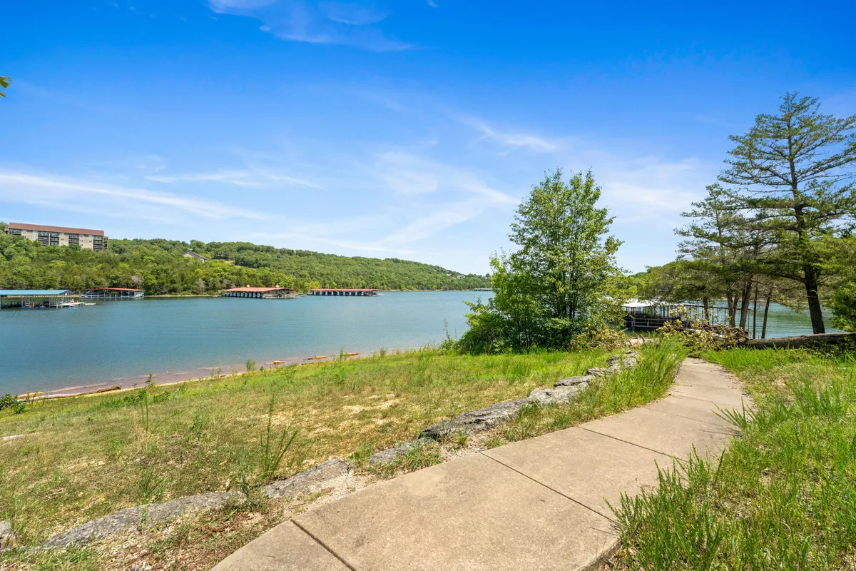 This image showcases a peaceful lake with a gently curving pathway surrounded by lush greenery. The scene highlights the natural beauty and opportunities for walking, fishing, or boating along the water's edge, with wildlife visible along the shore.