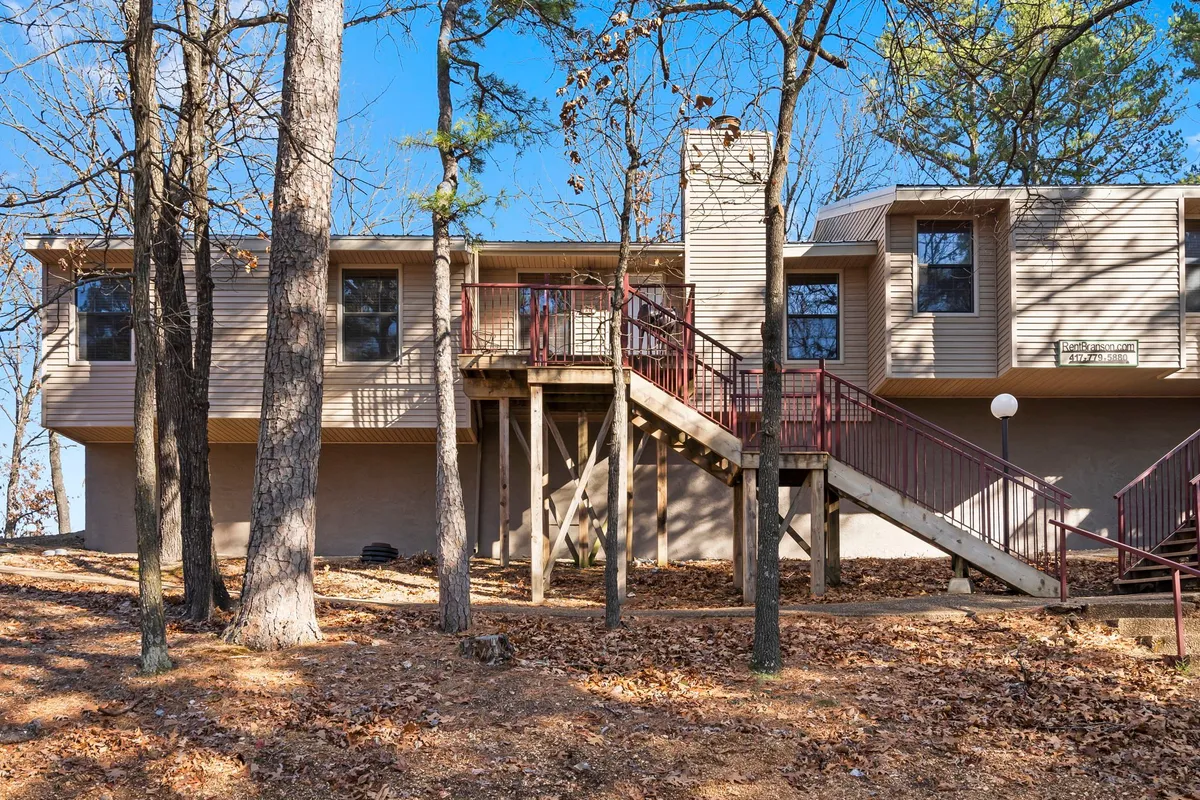 The exterior of a welcoming bungalow nestled among trees, with stairs leading up to a cozy deck. The setting suggests a peaceful, pet-friendly space for relaxing outdoors, enjoying sunsets, or hosting a barbecue.