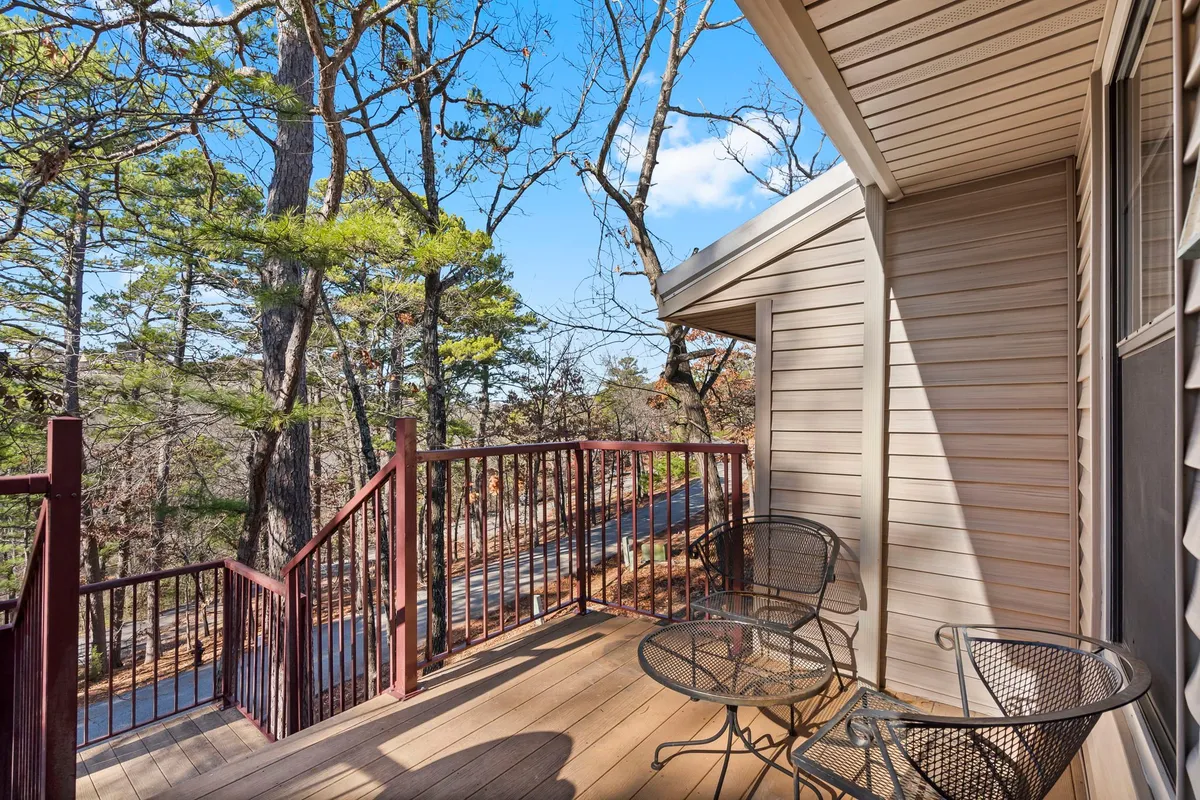 A private deck nestled amidst mature trees, with comfortable chairs overlooking a tranquil natural setting. The space is enclosed by greenery, perfect for unwinding with a pet, reading, or enjoying a peaceful morning outdoors.