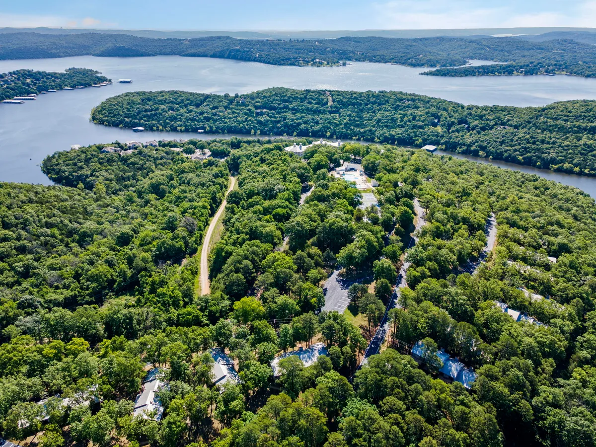 A wide exterior view of the lake framed by a lush surrounding forest, with a road and resort homes visible in the distance. The peaceful scene is ideal for walks, picnics, and lakeside exploration, offering a glimpse of the natural beauty accessible from the resort.