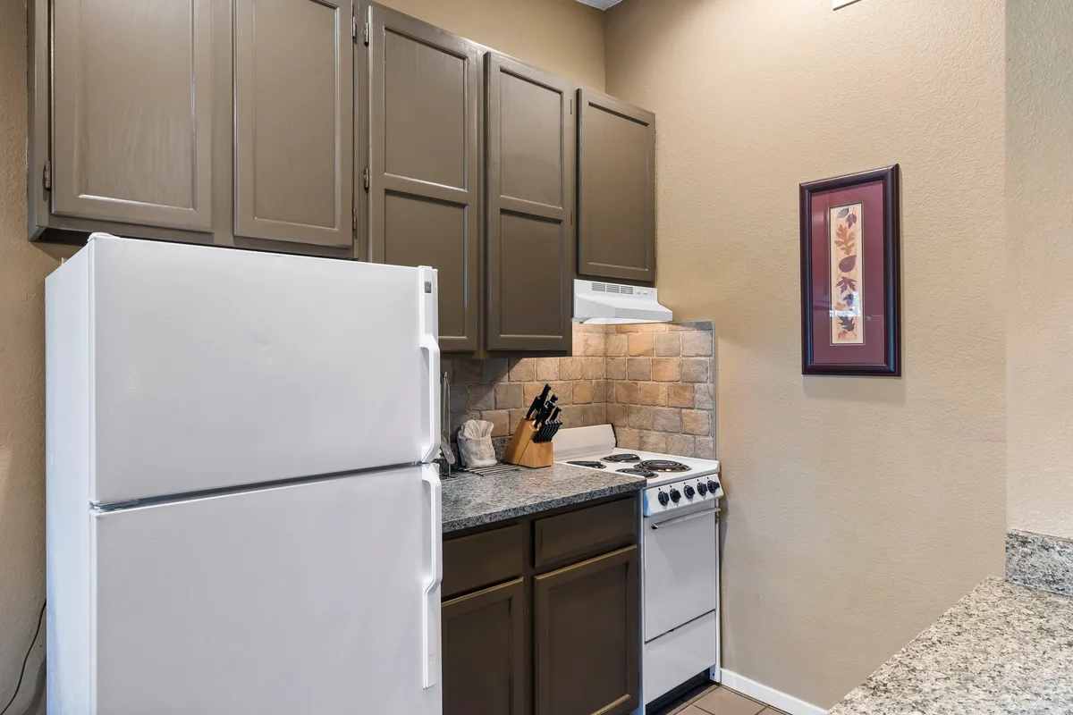 A practical yet cozy kitchen area with a refrigerator, stove, granite countertops, wood cabinetry, and tasteful decorative wall art. The atmosphere is ideal for meal prep, baking, and hosting small gatherings.