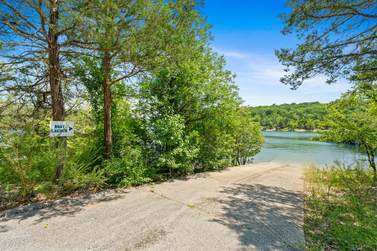 This image features a sign for the boat launch, a sparkling water surface, a lush tree line, and a convenient driveway approach. The boat launch area is clearly visible, inviting guests to embark on water adventures directly from the property, while the surrounding greenery enhances the sense of being close to nature.