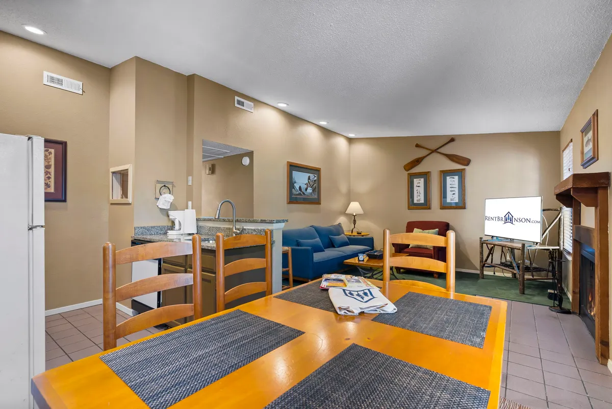 The image shows an open-concept living/dining area with a dining table, blue sofa, fireplace, and television. The space blends modern comfort with vintage charm and accommodates both relaxation and entertainment, capturing the multifunctional nature of the central hub.