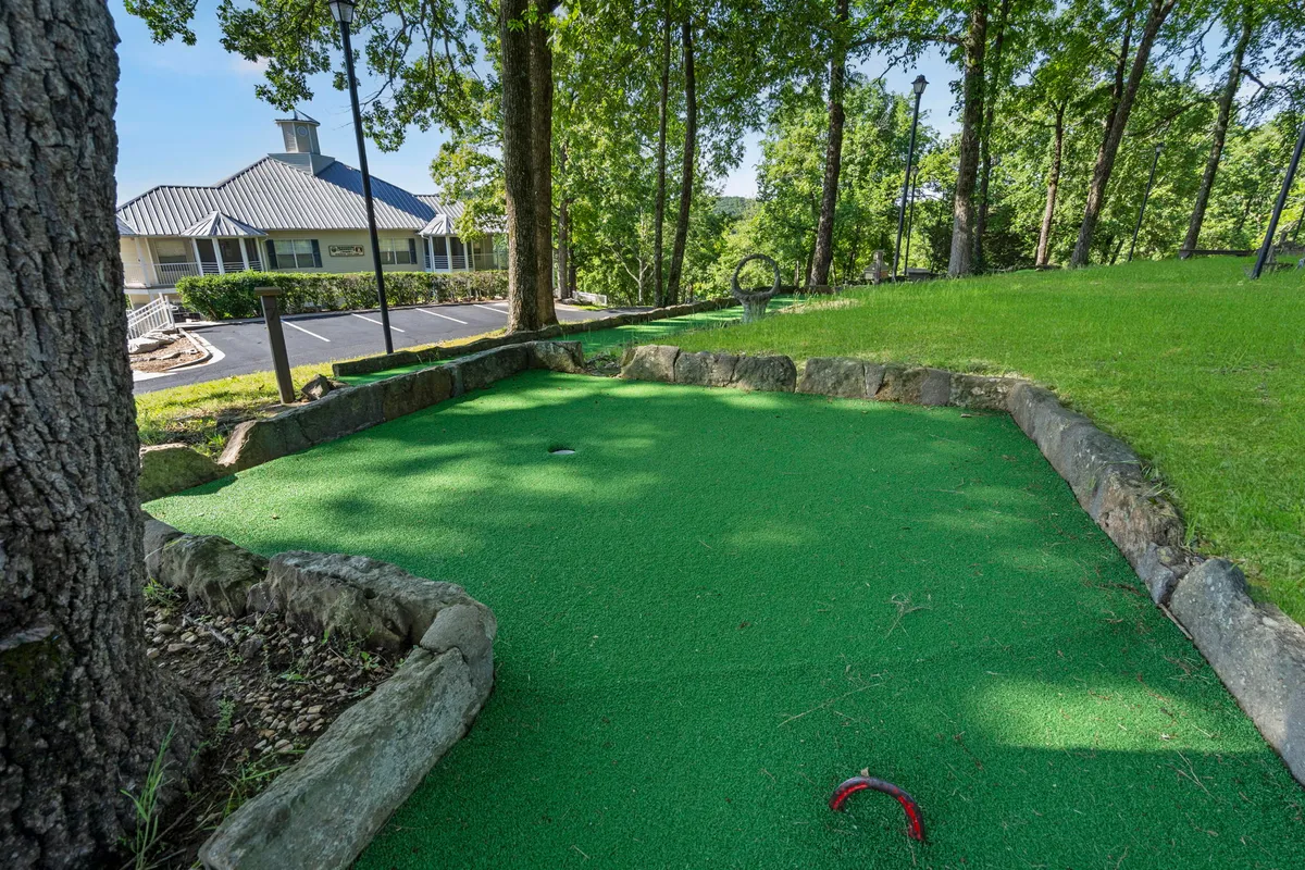 A vibrant mini-golf area surrounded by lush greenery and bordered by stone edging. The scene is set outdoors, with winding paths and colorful putting greens inviting families to gather and play. The landscape offers a scenic and playful environment perfect for family outings.