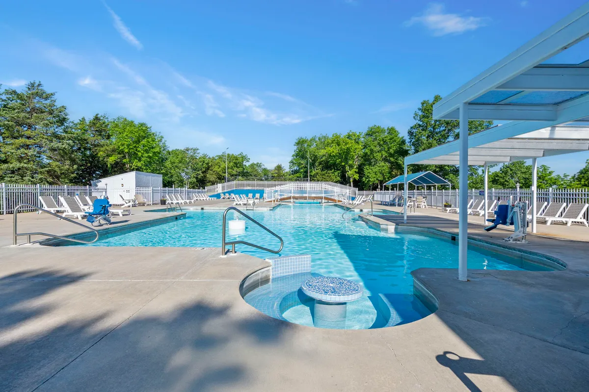 A vibrant resort swimming pool area, featuring a jacuzzi, plenty of lounge chairs, and shaded spots for relaxation. The pool is lively, ideal for families and friends enjoying a cheerful atmosphere under the sun.